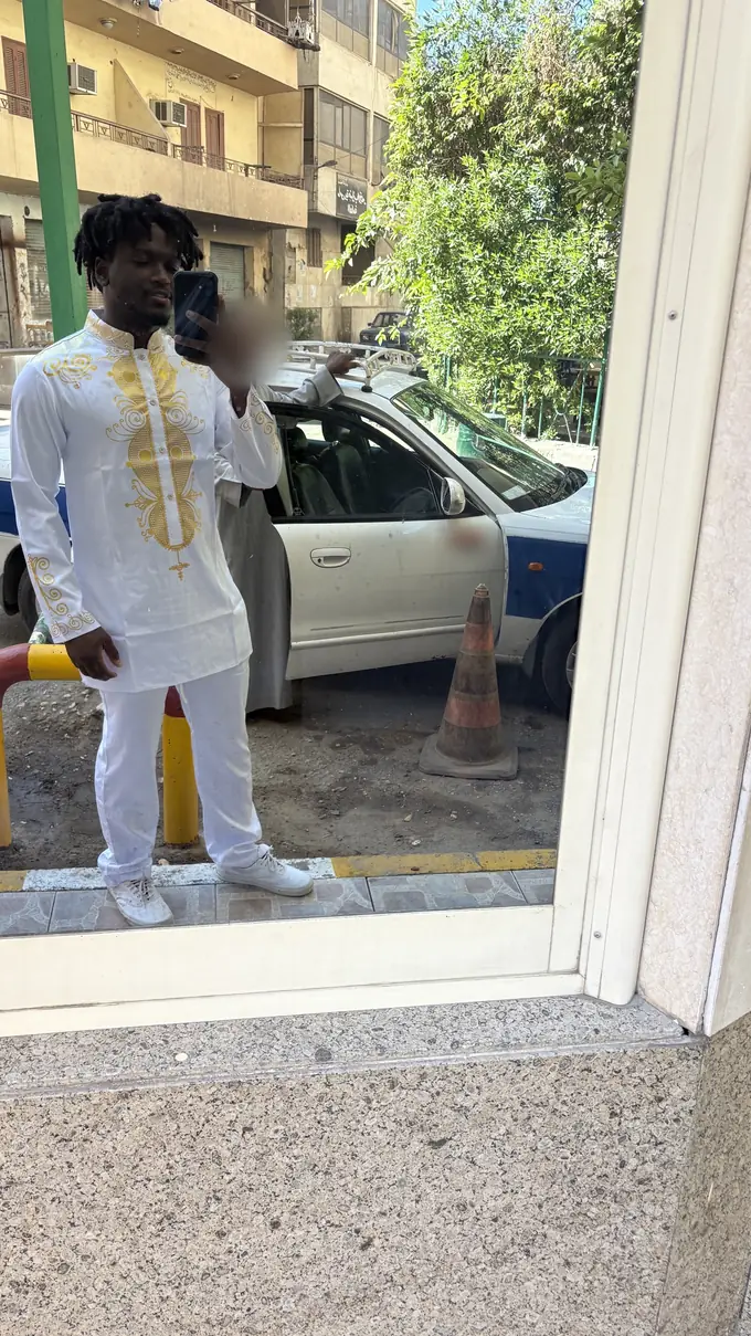 The site owner in the same white and gold outfit, taking a mirror selfie outdoors in Egypt, with a parked taxi behind.