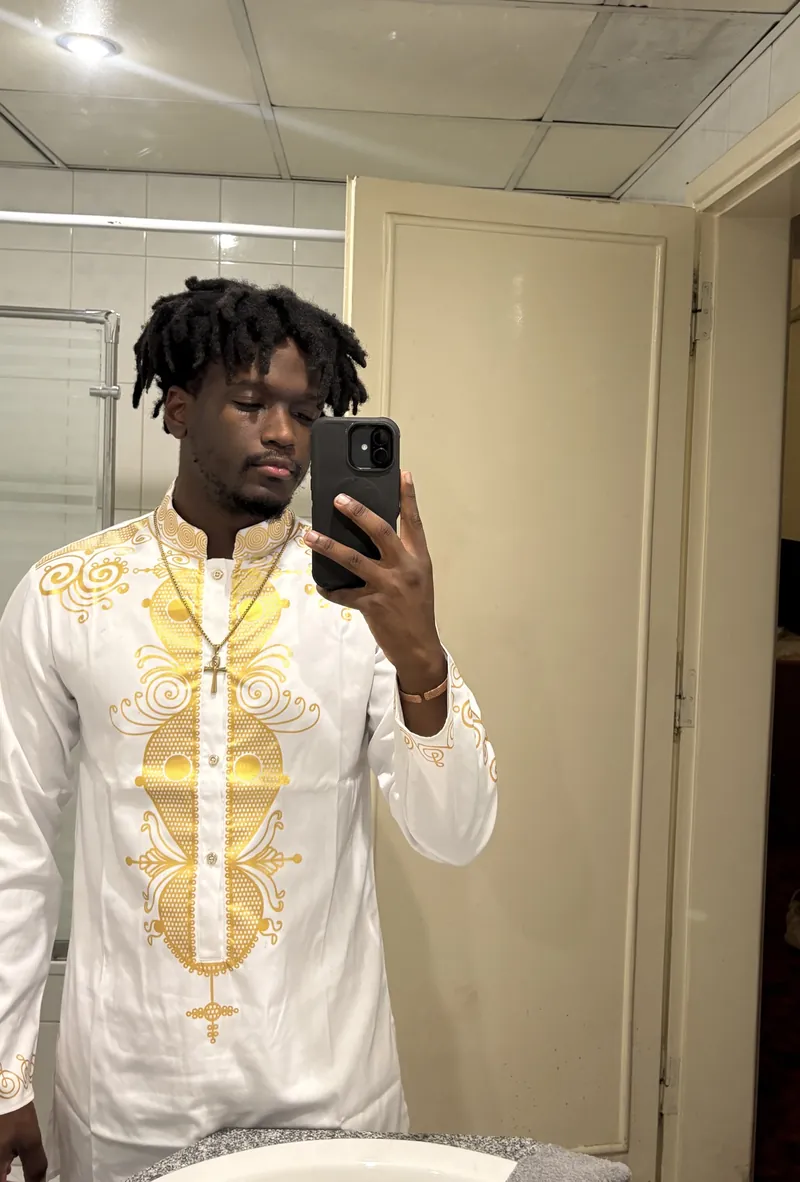 The site owner in the white and gold embroidered outfit with a gold cross necklace, taking a mirror selfie.