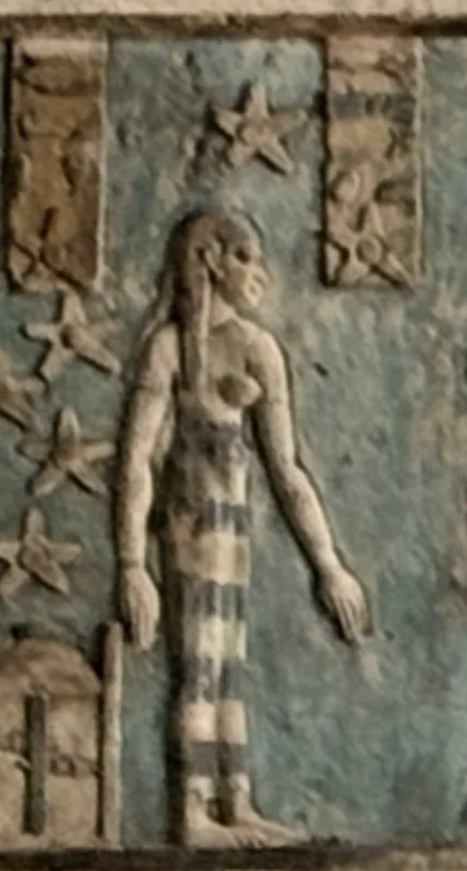 A frontal standing female figure carved in relief on a blue ground, bare to the waist, with long hair and a striped lower garment, with several stars around one side of her and above her.