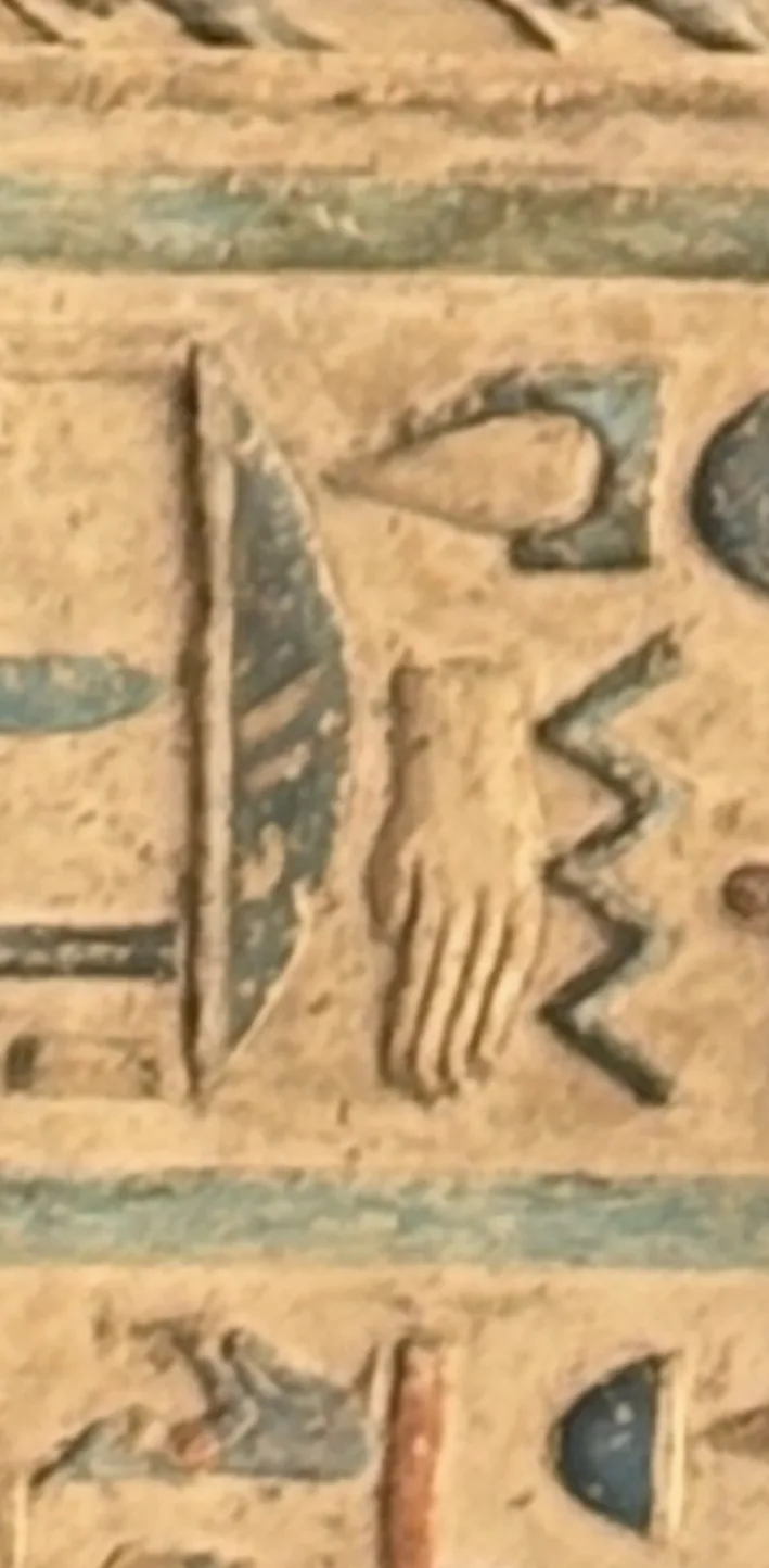 A close-up of painted relief on a sand-coloured ground: a hand sign, a zigzag sign and a tall curved blade-like sign, with a blue-green drop-like form at the upper right and a blue-green band across the top.