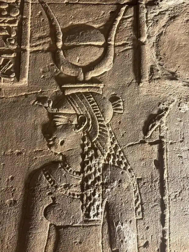 A carved relief of a goddess in profile wearing a crown of a sun disc between cow horns, set on a modius, with a long patterned wig.
